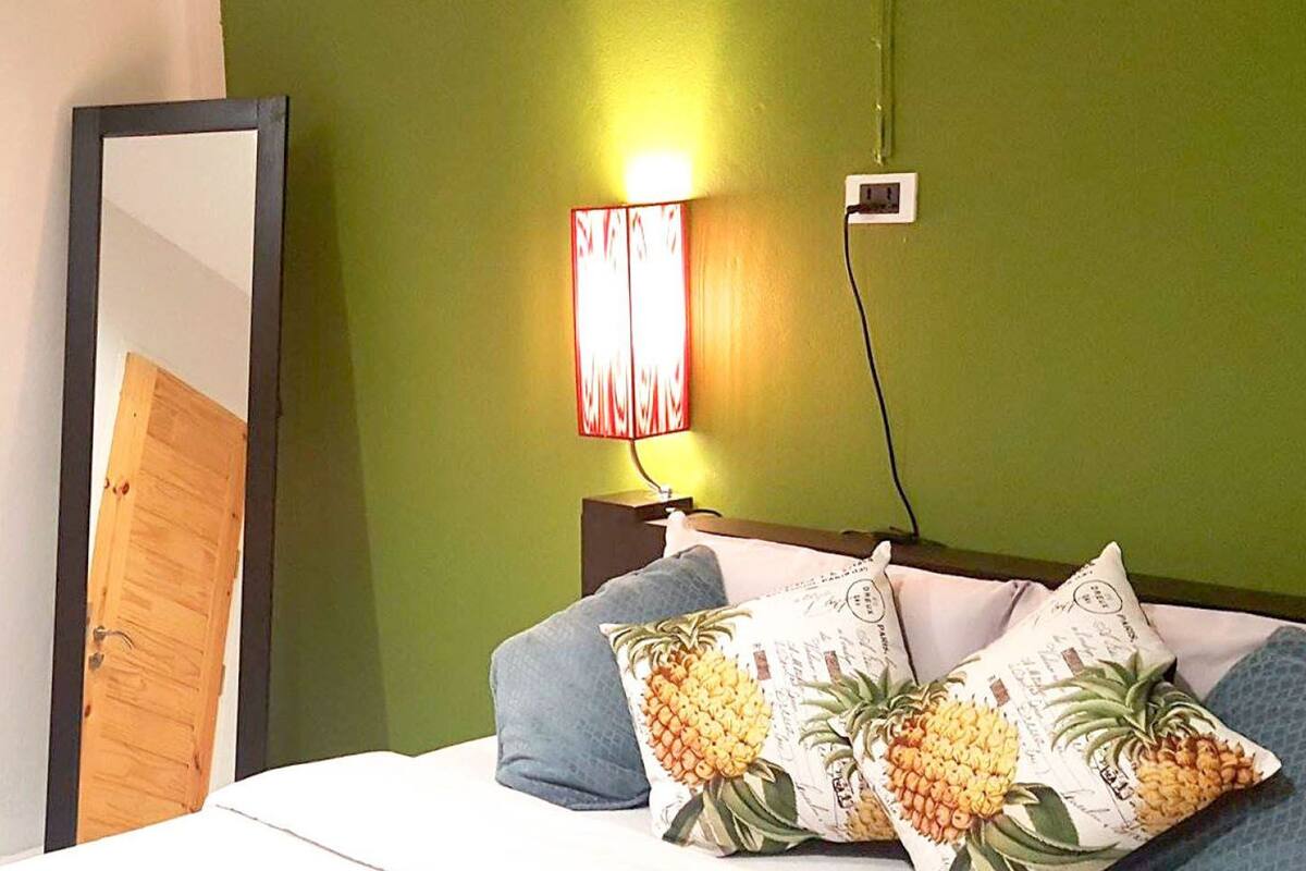 A hotel room with a bed, pillows, a nightstand, a wall-mounted lamp, and a mirror.