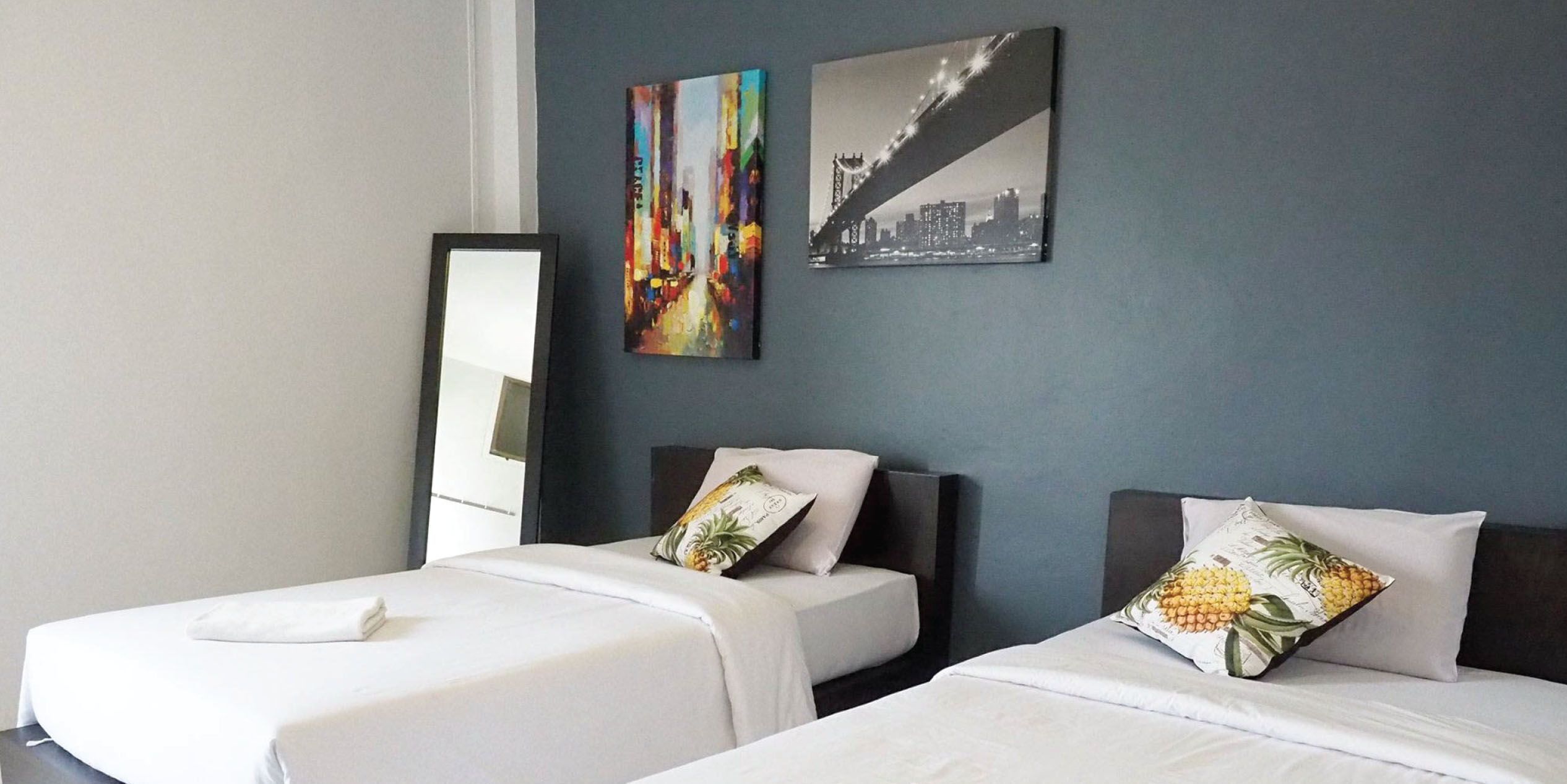 A hotel room with two beds, a large mirror, and two wall-mounted artworks.