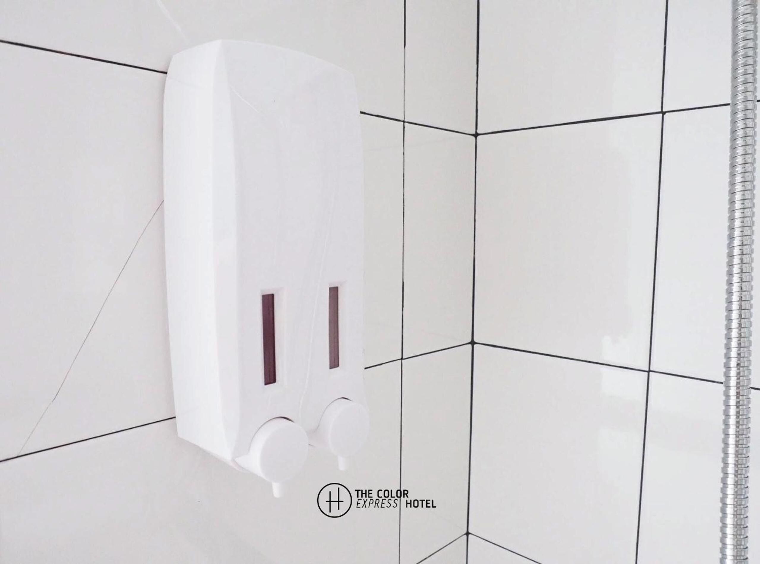 A white wall-mounted soap dispenser with two buttons, set against a tiled wall with a geometric pattern.