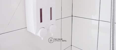 A white wall-mounted soap dispenser with two buttons, set against a tiled wall with a geometric pattern.