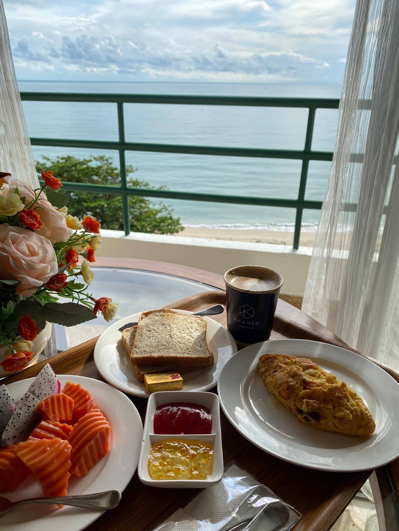 A breakfast tray with toast, coffee, omelette, and various condiments on a balcony overlooking the sea.