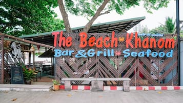 A beachside restaurant named "The Beach Khamon Bar & Grill" with a signboard and outdoor seating area.