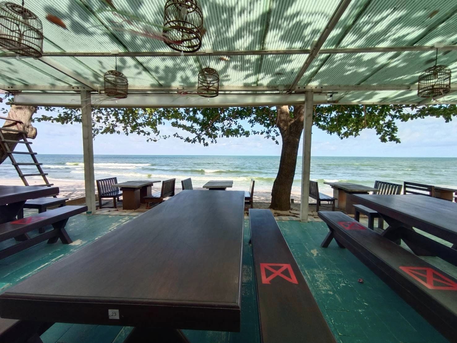 A beachside café with outdoor seating under a shaded canopy, overlooking the ocean.