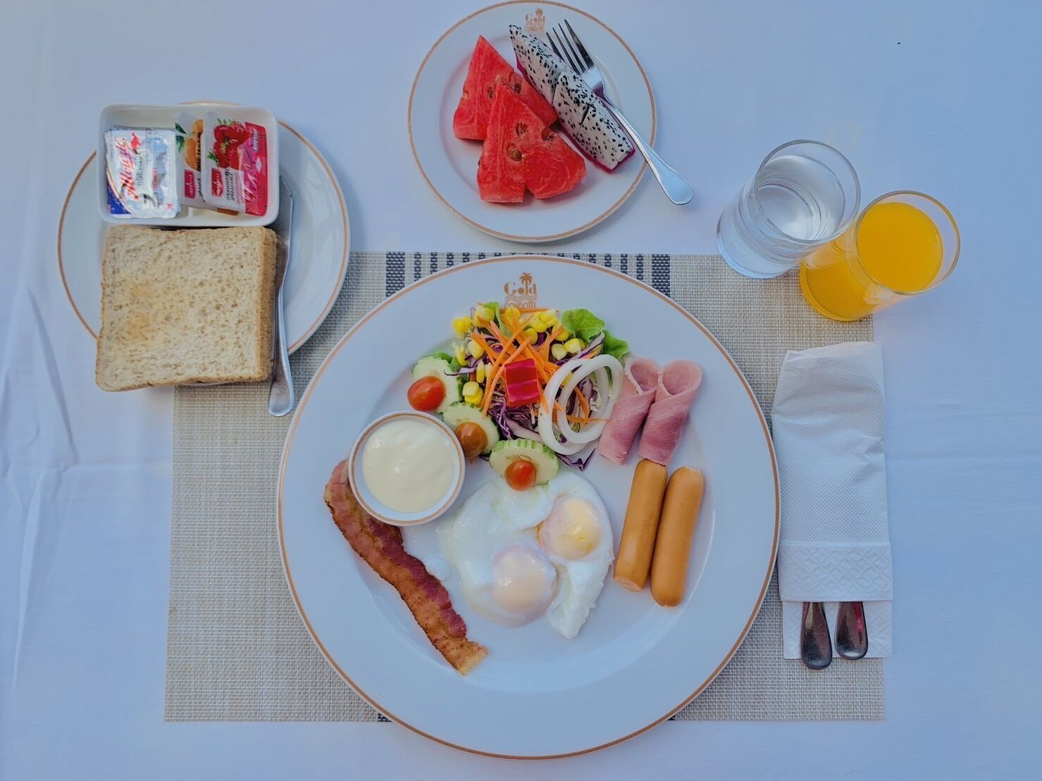 A breakfast plate with eggs, bacon, sausages, a salad, and a slice of toast.