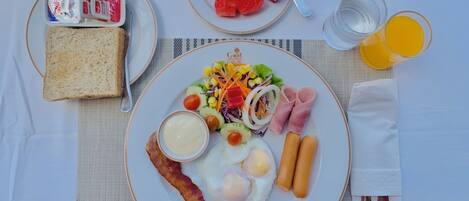 A breakfast plate with eggs, bacon, sausages, a salad, and a slice of toast.