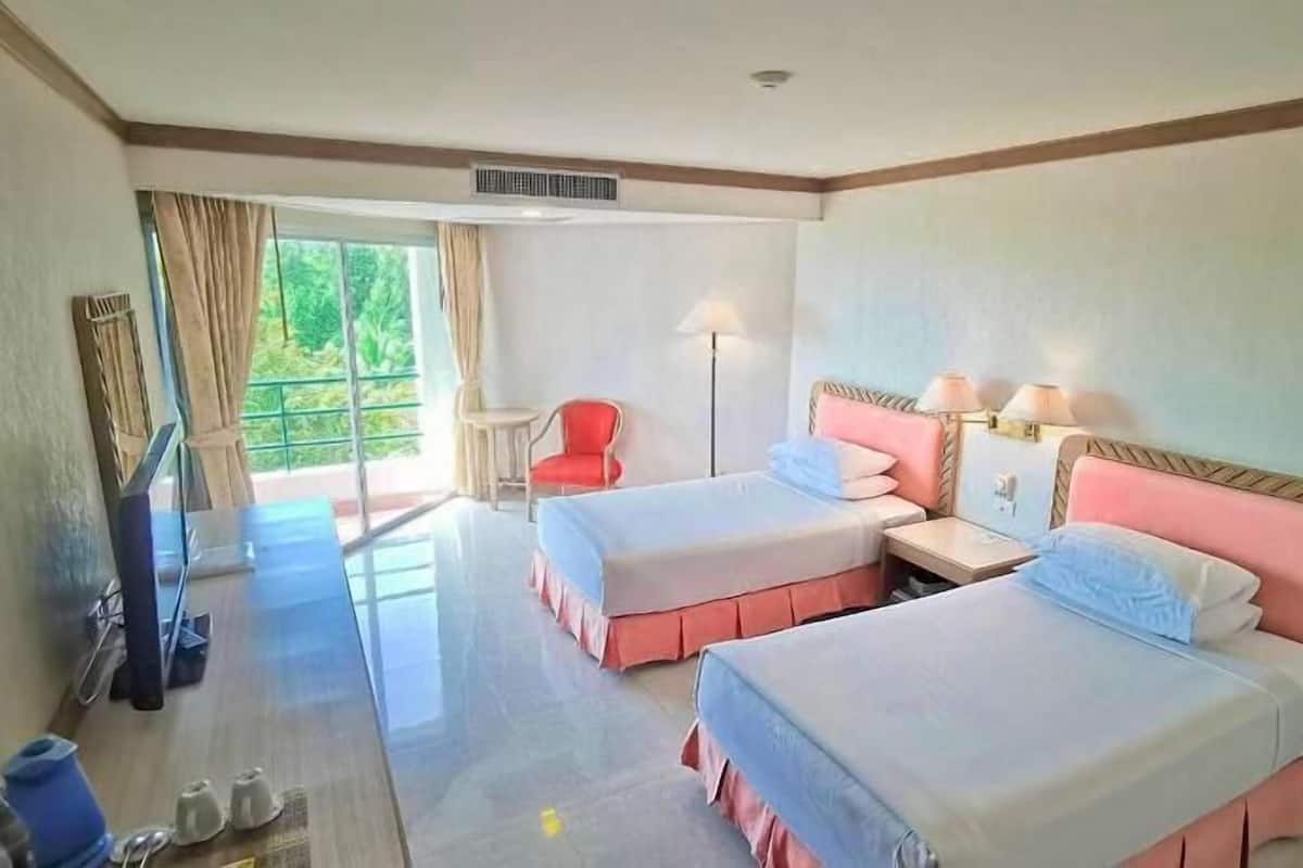 Une chambre d’hôtel avec deux lits, une télévision, une chaise et un balcon avec des rideaux.