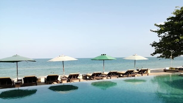 Une piscine à débordement à l’eau d’un bleu cristallin, entourée de chaises longues et de parasols, avec une vue imprenable sur l’océan.