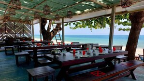 Un espace extérieur aménagé pour les repas, avec des tables et des bancs en bois, donnant sur une plage.