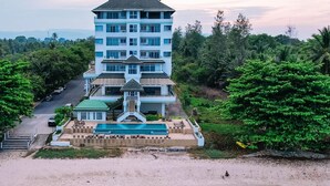 Un hôtel à plusieurs étages doté d’une piscine, entouré d’une végétation luxuriante et offrant une vue dégagée sur la route.
