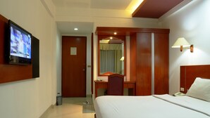 Una habitación de hotel con una cama, un escritorio con silla, un televisor montado en la pared y una lámpara.