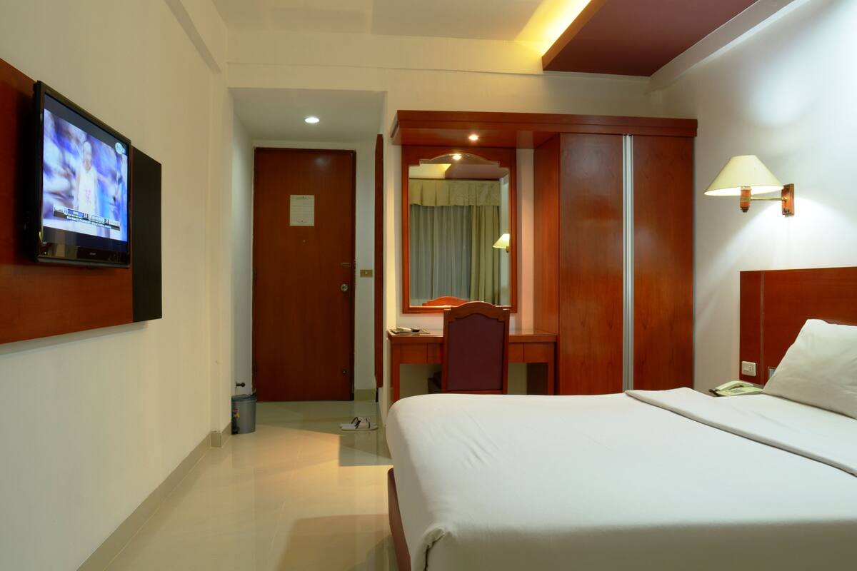 Una habitación de hotel con una cama, un escritorio con silla, un televisor montado en la pared y una lámpara.