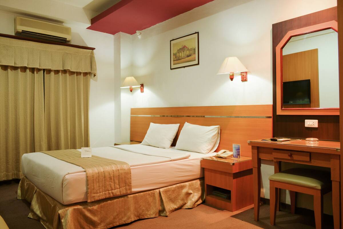 Una habitación de hotel con cama, mesita de noche, silla, escritorio y espejo.