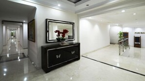 Un moderno vestíbulo de hotel con un largo pasillo, una consola negra con adornos y una zona de recepción con una escalera.