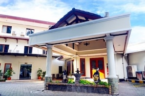 A covered outdoor area with a fountain, potted plants, and a building entrance.
