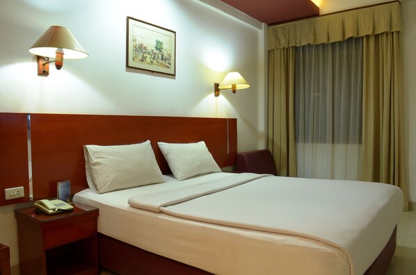 A hotel room with a large bed, two bedside lamps, a nightstand with a phone, and a window with curtains. - Hotel Puri Mega (Jakarta)