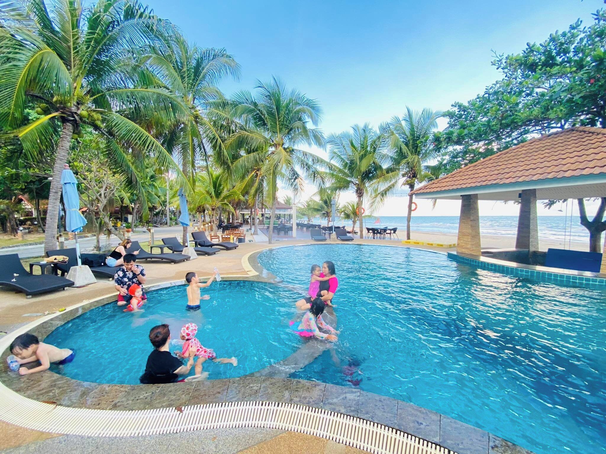Una piscina rodeada de palmeras y sillas de descanso, con vista a la playa.