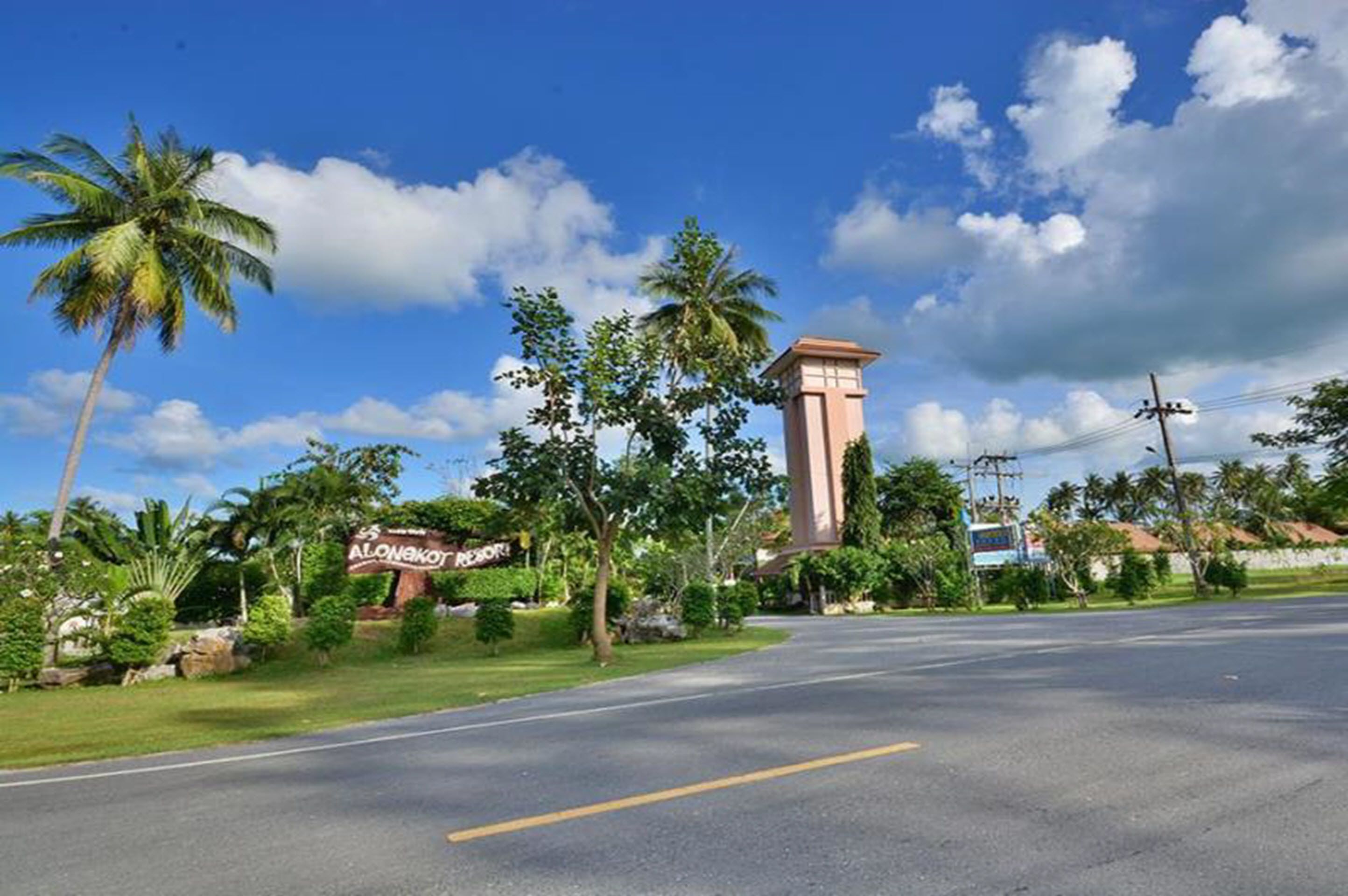 A road leading to a building with a sign that reads "Alonako Resort."