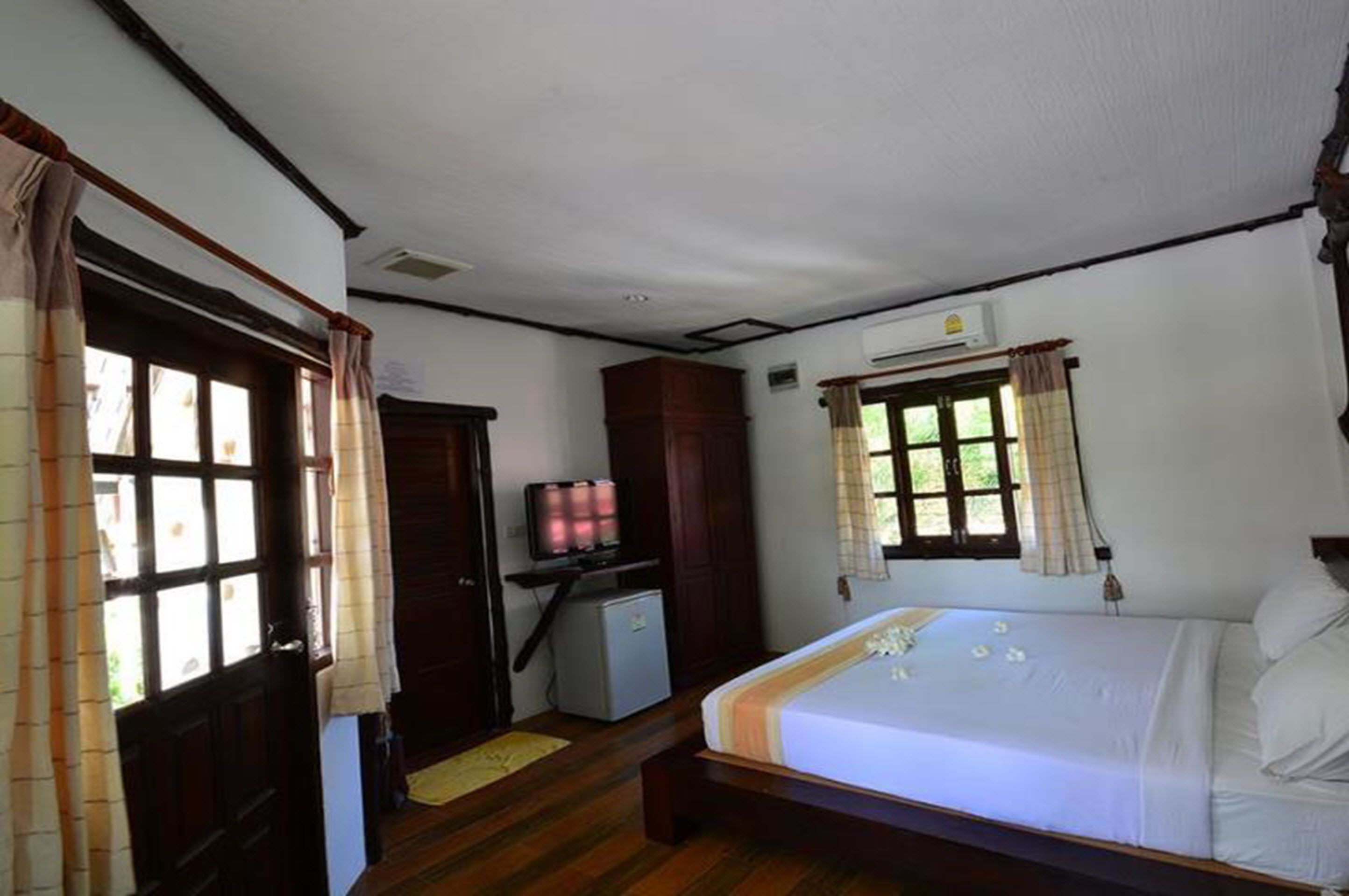 Un dormitorio con cama, escritorio con televisor, armario y ventana con cortinas.