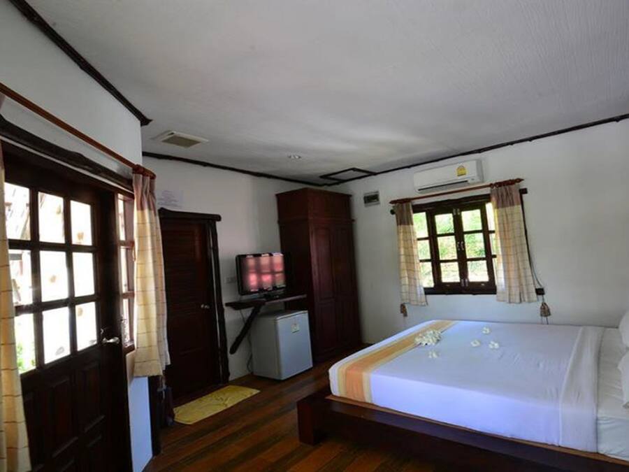 Un dormitorio con cama, escritorio con televisor, armario y ventana con cortinas.