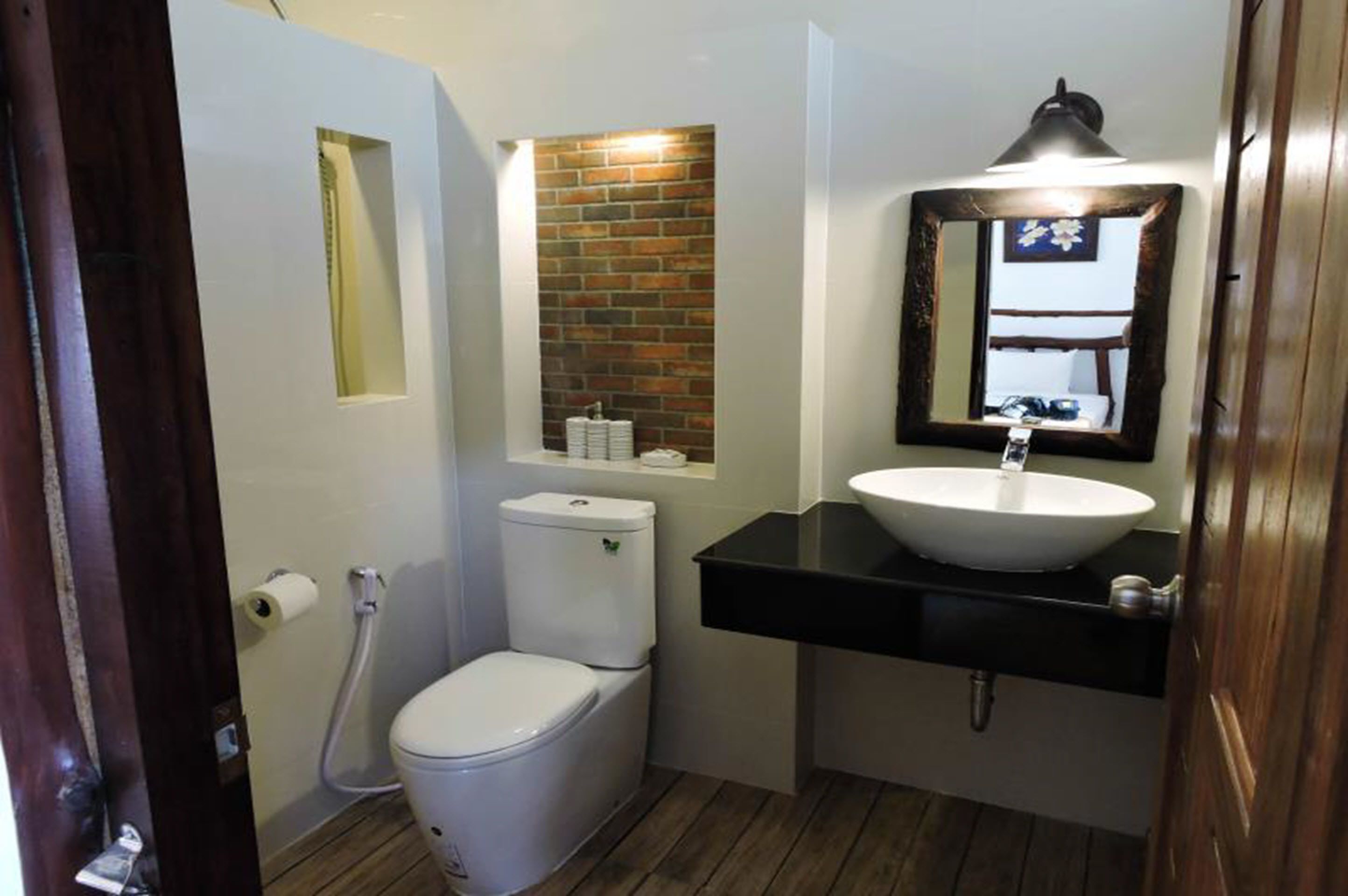 A compact bathroom with a white toilet, a black sink, and a mirror above it.