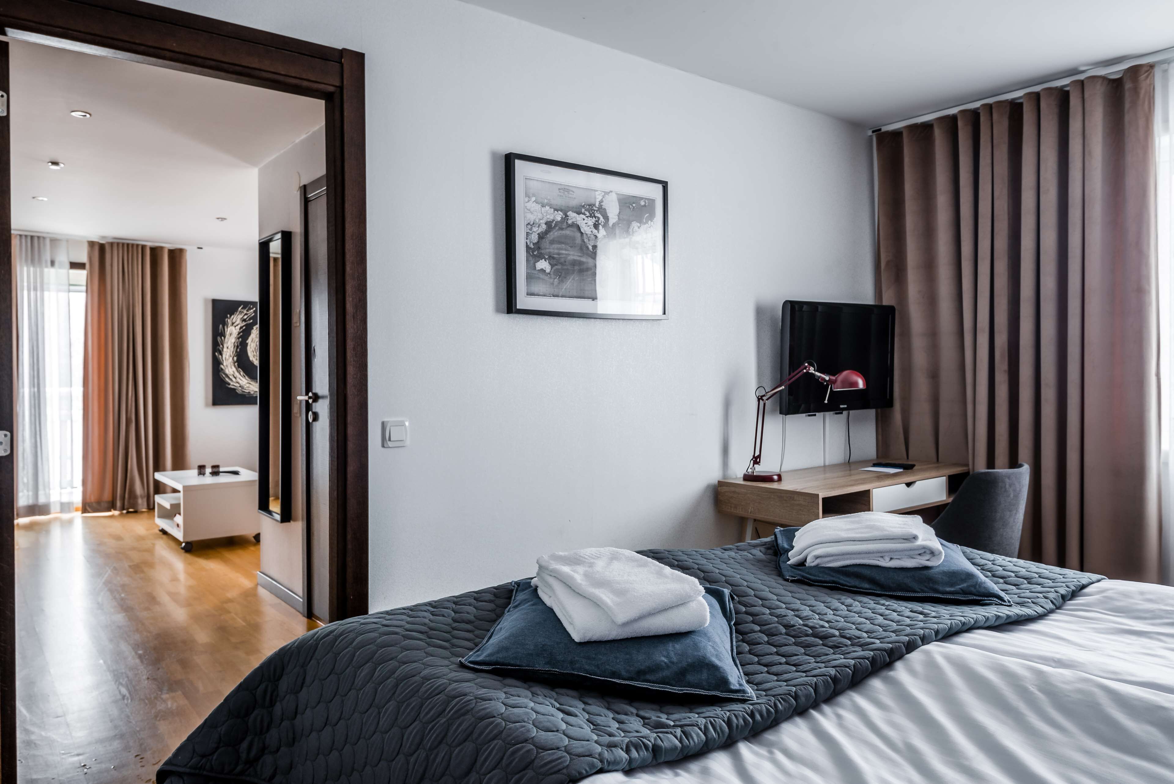 Una habitación de hotel moderna con cama, escritorio, televisión y baño visible a través de una puerta abierta.