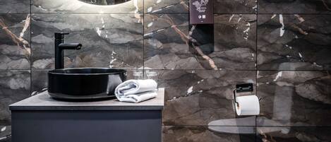 A modern bathroom with a black sink, marble tiles, a towel, and a toilet paper holder.