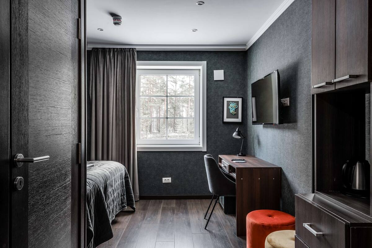 Un dormitorio moderno con un gran ventanal, un escritorio, una silla, un televisor y un armario.