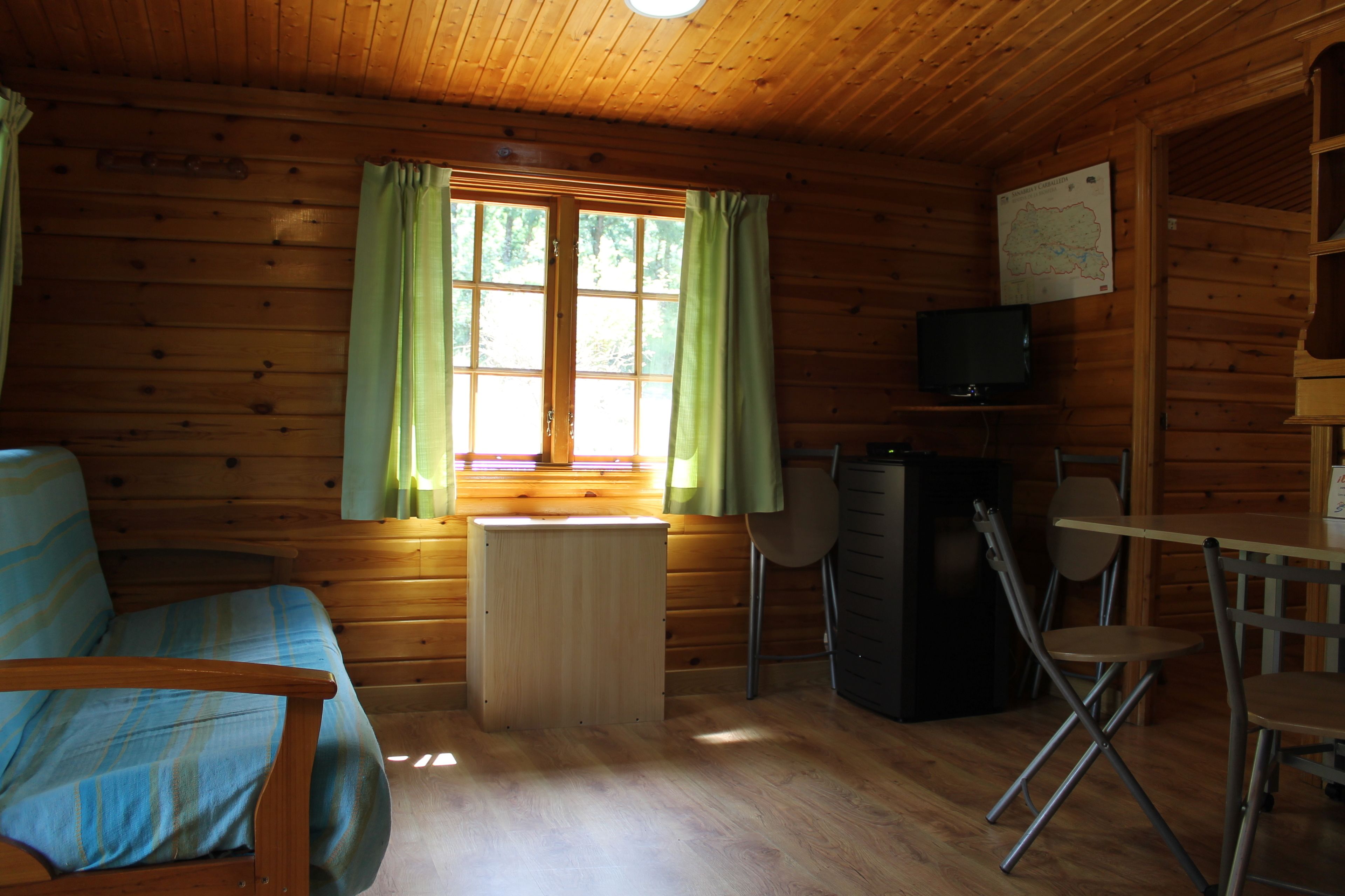 A wooden cabin interior with a sofa, a small table, a TV, and a map on the wall.