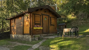 Una cabaña de madera con cimientos de piedra, un pequeño porche y una mesa con sillas afuera.