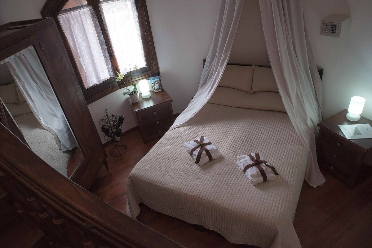A bedroom with a bed, a bedside table, a nightstand, a mirror, and a window with curtains.