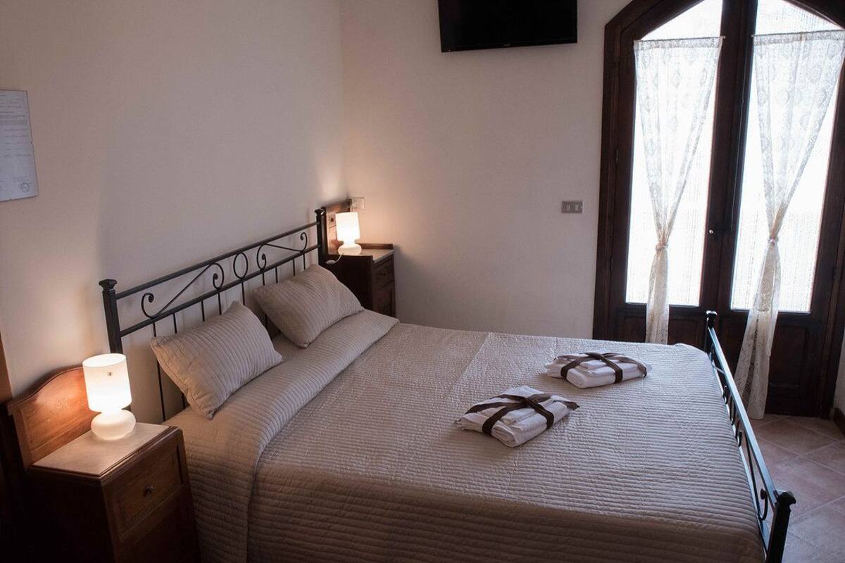 A neatly made bed with a headboard, a bedside lamp, and two towels on the bed.