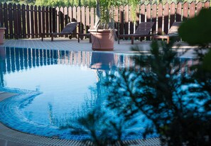 A swimming pool with a wooden deck, lounge chairs, and a wooden fence in the background. - Il Castello (Piazza Armerina)