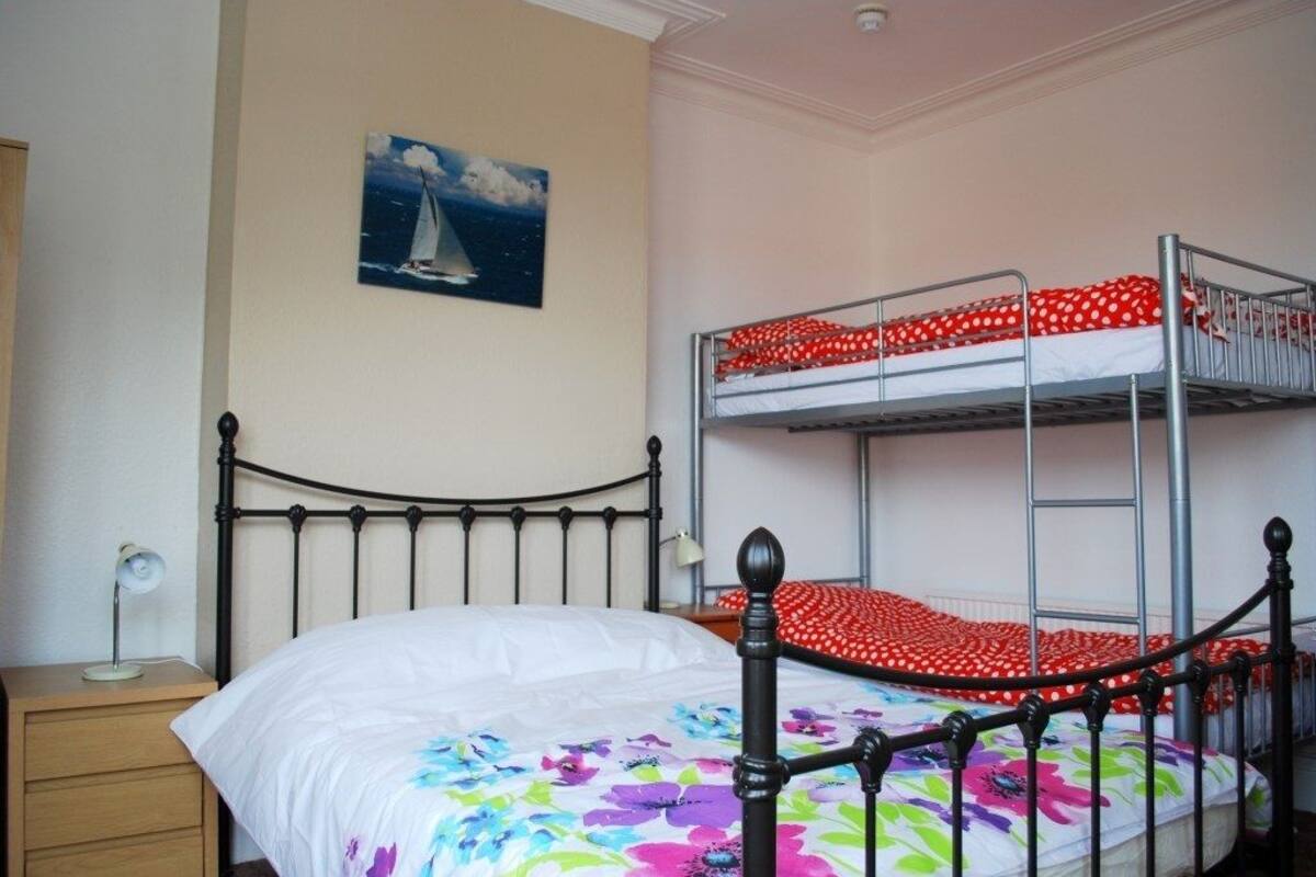 A bedroom with a single bed, a bunk bed, a nightstand, a lamp, and a painting of a sailboat.