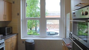 A kitchen with a window, wooden cabinets, a microwave, an oven, and a trash can. - Clift Guest House (Bristol)