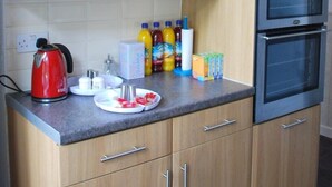 A kitchen with wooden cabinets, a built-in oven, a kettle, and various kitchen items on the counter. - Clift Guest House (Bristol)