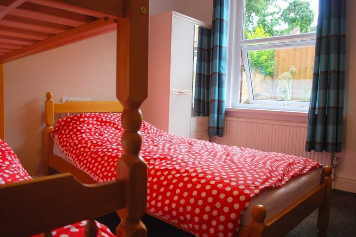 A bedroom with a wooden four-poster bed, a white wardrobe, and a window with curtains.