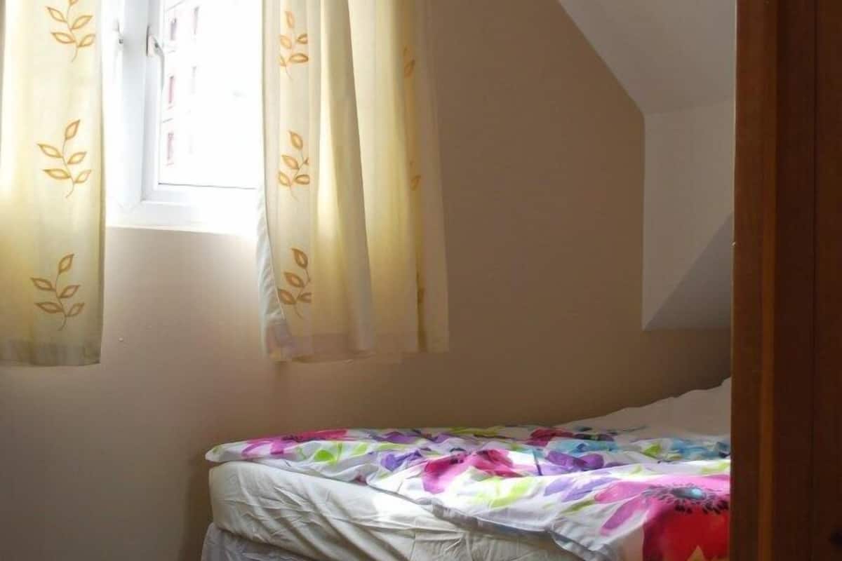 A bedroom with a sloped ceiling, a window with curtains, a bed with a colorful bedspread, and a carpeted floor.