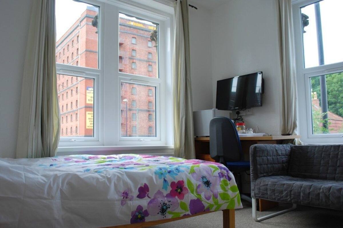 A hotel room with a bed, a desk with a computer, a TV, and a view of a red brick building.