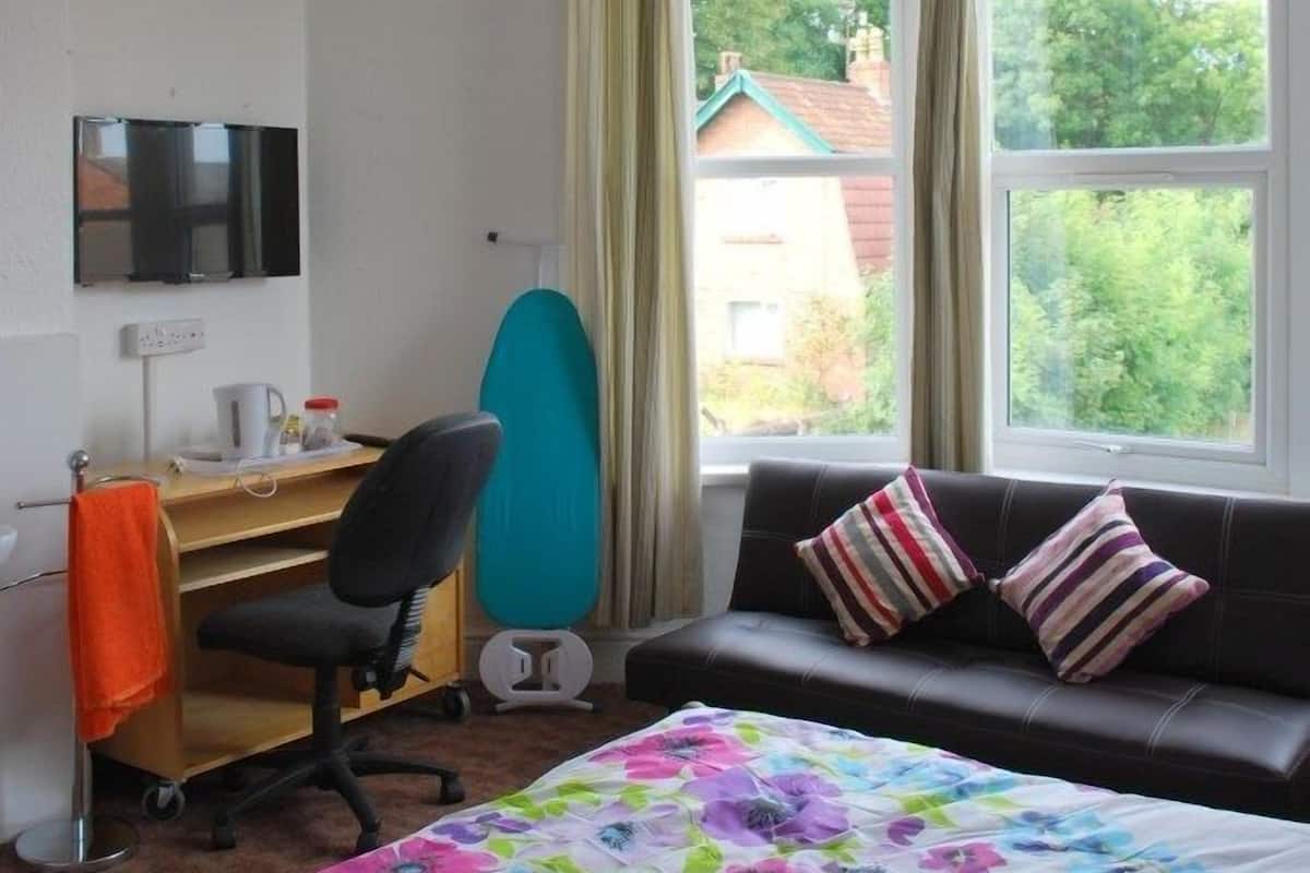A hotel room with a bed, a desk with a chair, a television, and a window with curtains.