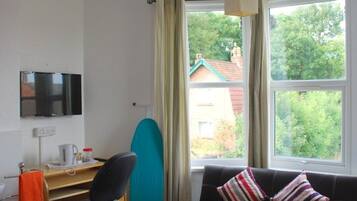 Hotellihuone, jossa on sänky, työpöytä, tuoli, televisio ja ikkuna, josta avautuu näkymä vehreään maisemaan.