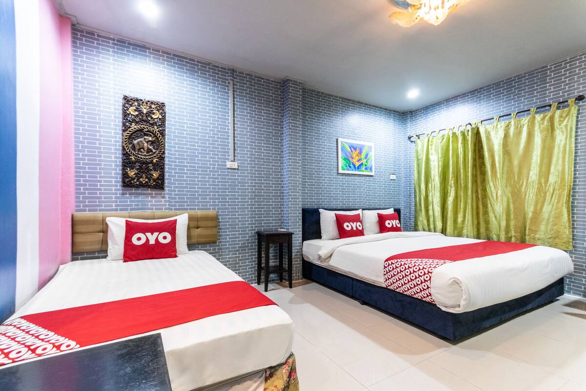 A hotel room with two beds, a brick-patterned wall, a small table, and a green curtain.