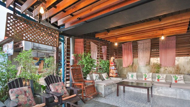 A cozy outdoor seating area with wooden furniture, a concrete floor, and a mix of plants and decorative elements. - OYO 75304 Riverside Guesthouse (Takua Pa)