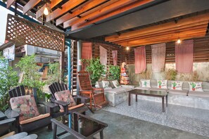 A cozy outdoor seating area with wooden furniture, a concrete floor, and a mix of plants and decorative elements. - OYO 75304 Riverside Guesthouse (Takua Pa)