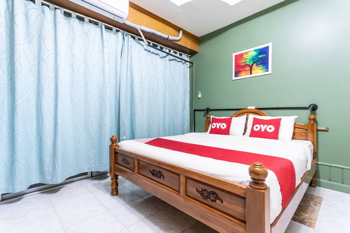 A neatly made bed with a red and white bedspread, two pillows with the word "OYO" on them, and a wooden headboard.