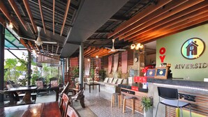 A restaurant interior with wooden tables and chairs, a bar area, and a wall with the logo 'RIVERSID'. - OYO 75304 Riverside Guesthouse (Takua Pa)