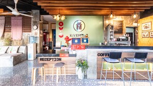 A coffee shop interior with a reception desk, seating area, and a counter with a menu board. - OYO 75304 Riverside Guesthouse (Takua Pa)
