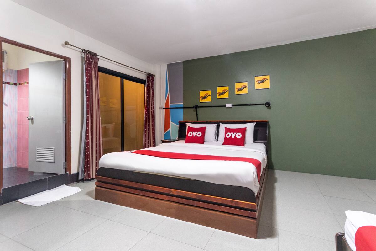 A hotel room with a large bed, a sliding door, and a green wall with three framed pictures.
