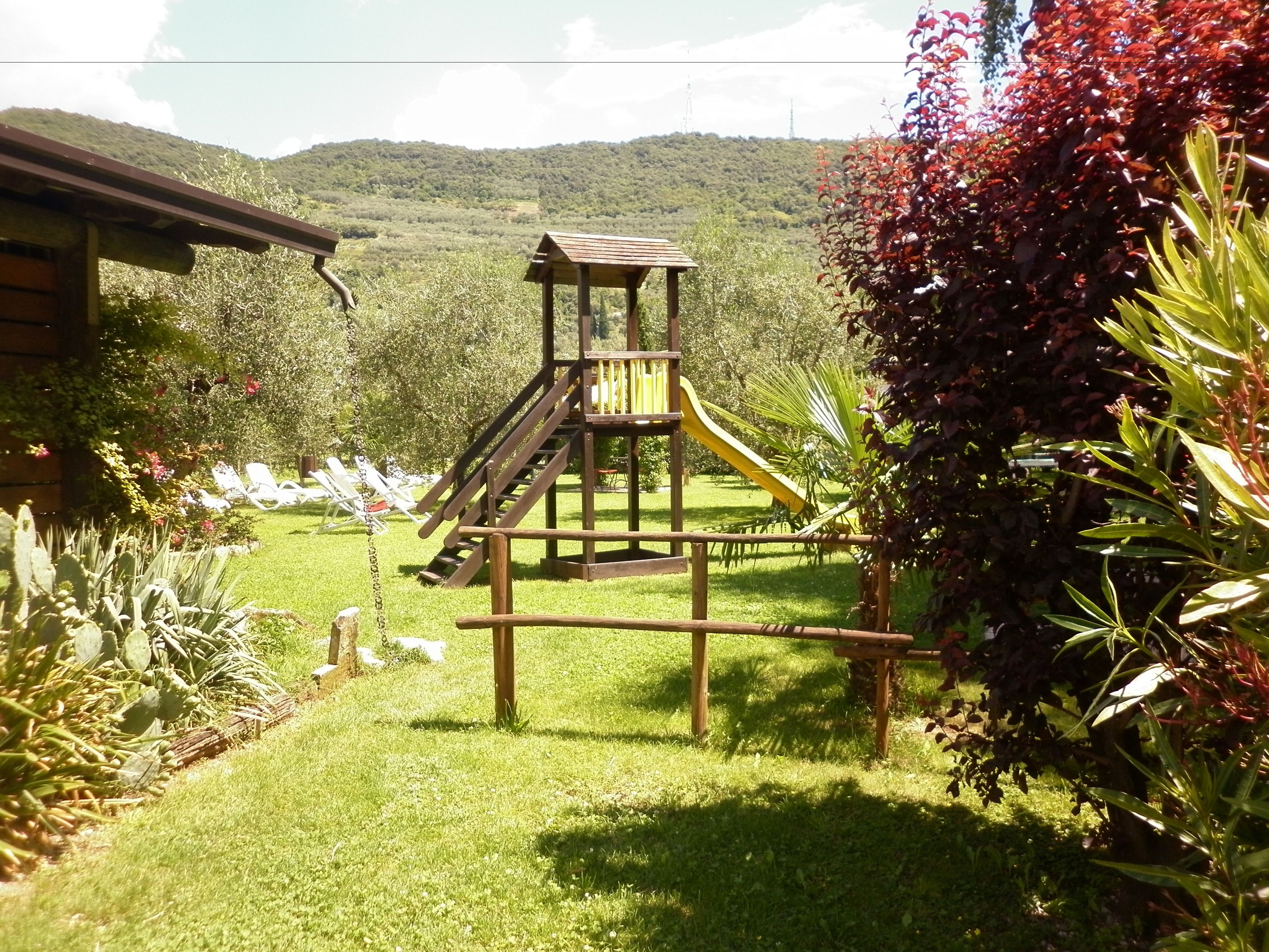 A wooden play structure with a slide in a grassy area with a mountain backdrop.