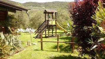 A wooden play structure with a slide in a grassy area with a mountain backdrop.