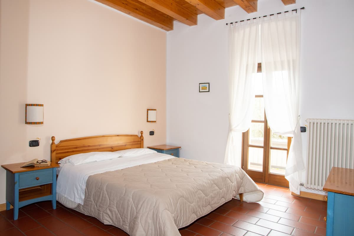 Une chambre à coucher avec un lit en bois, deux tables de chevet, une commode, une fenêtre avec des rideaux et un radiateur.